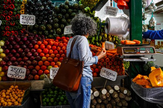 Woman shopping at a vibrant local market stall filled with fresh fruits and vegetables.