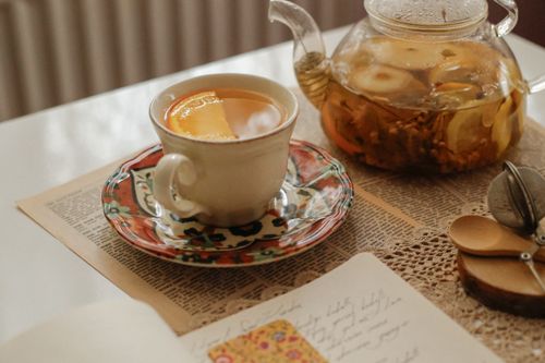 Free Warm homey scene of tea in a cup and glass teapot on a table with knit cloth and spoon. Stock Photo