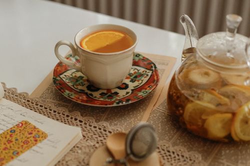 Free A warm, inviting setup featuring a teacup with orange slice and teapot on a lace tablecloth, evoking comfort. Stock Photo