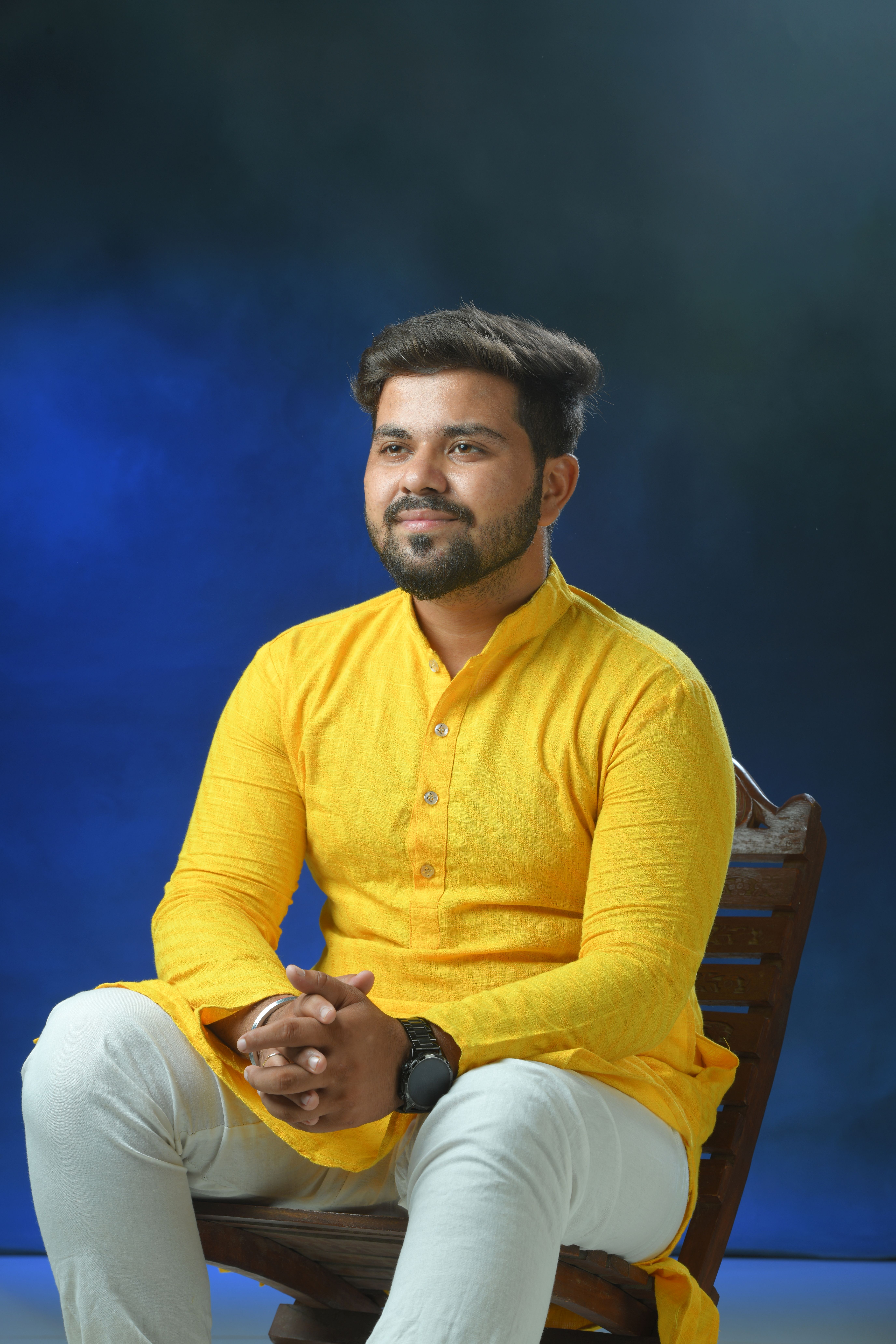A smiling man in a yellow kurta sits in a studio setting, exuding cultural elegance.