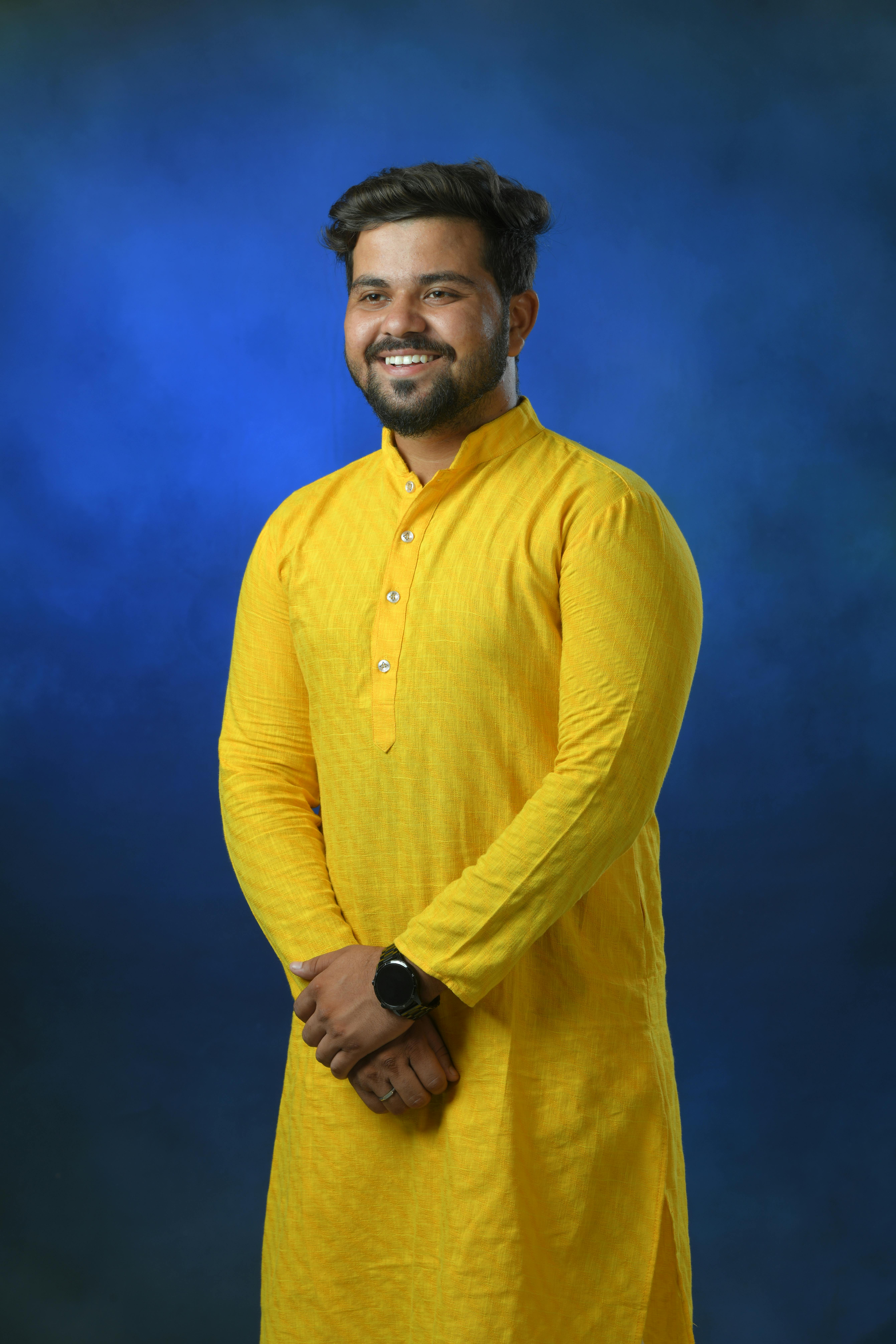 Portrait of a smiling man in a traditional yellow kurta against a blue background.
