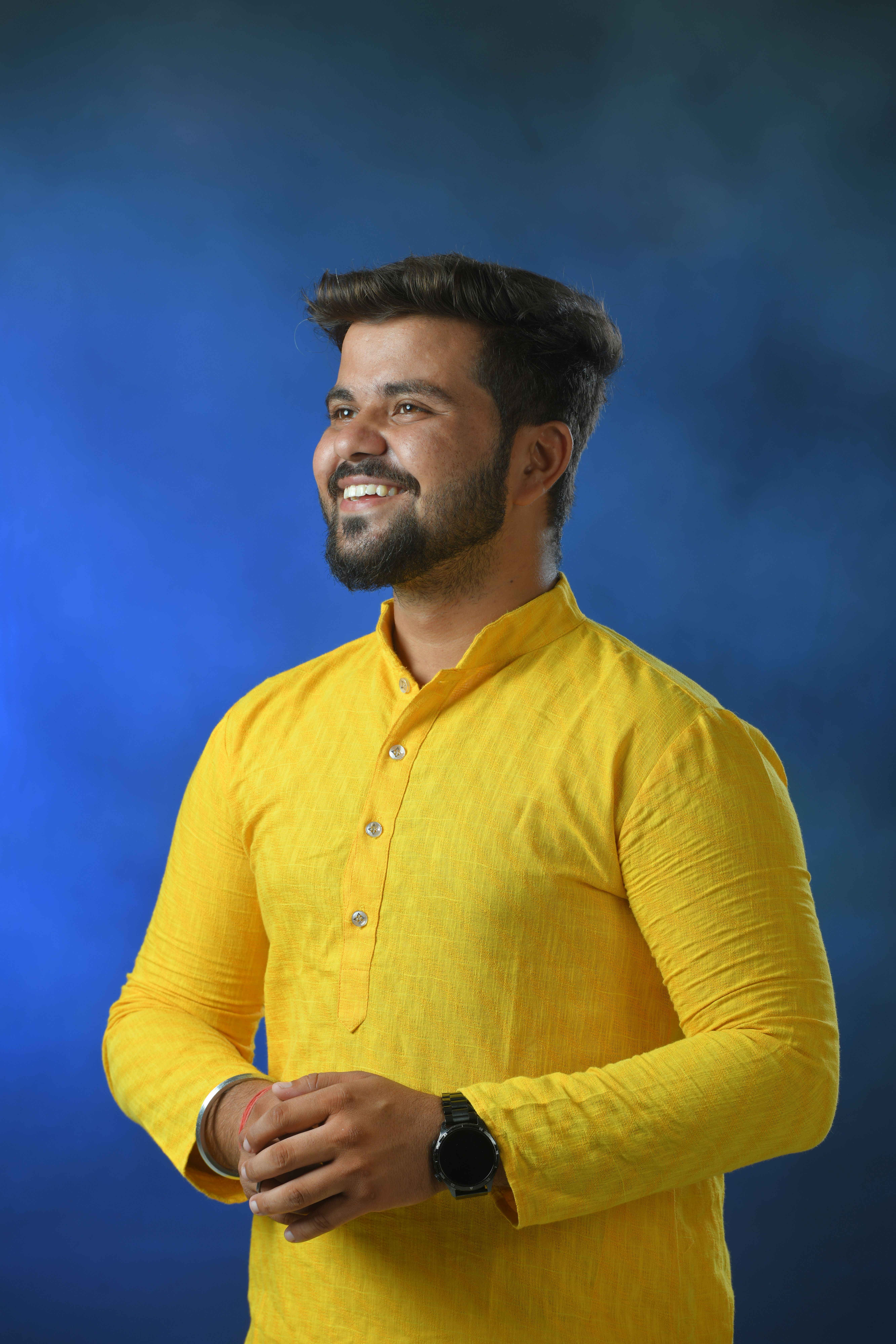 Portrait of a smiling man in a vibrant yellow kurta with a blue background