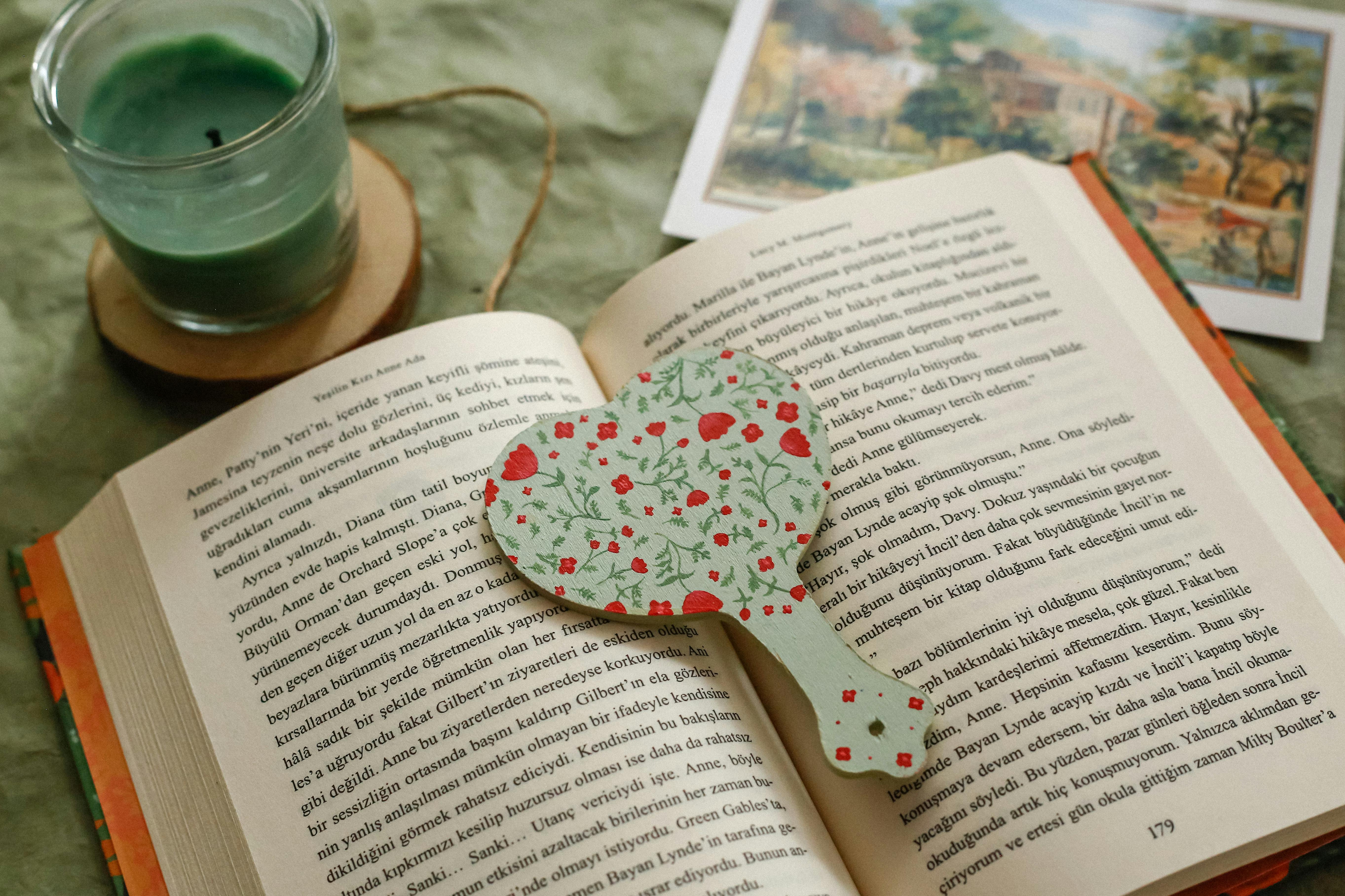 Open book on a green cloth with heart-shaped bookmark and green candle, perfect reading ambiance.