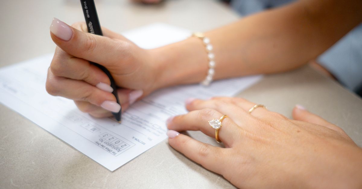 Detailed view of hands filling out a form with elegant jewelry and manicure.