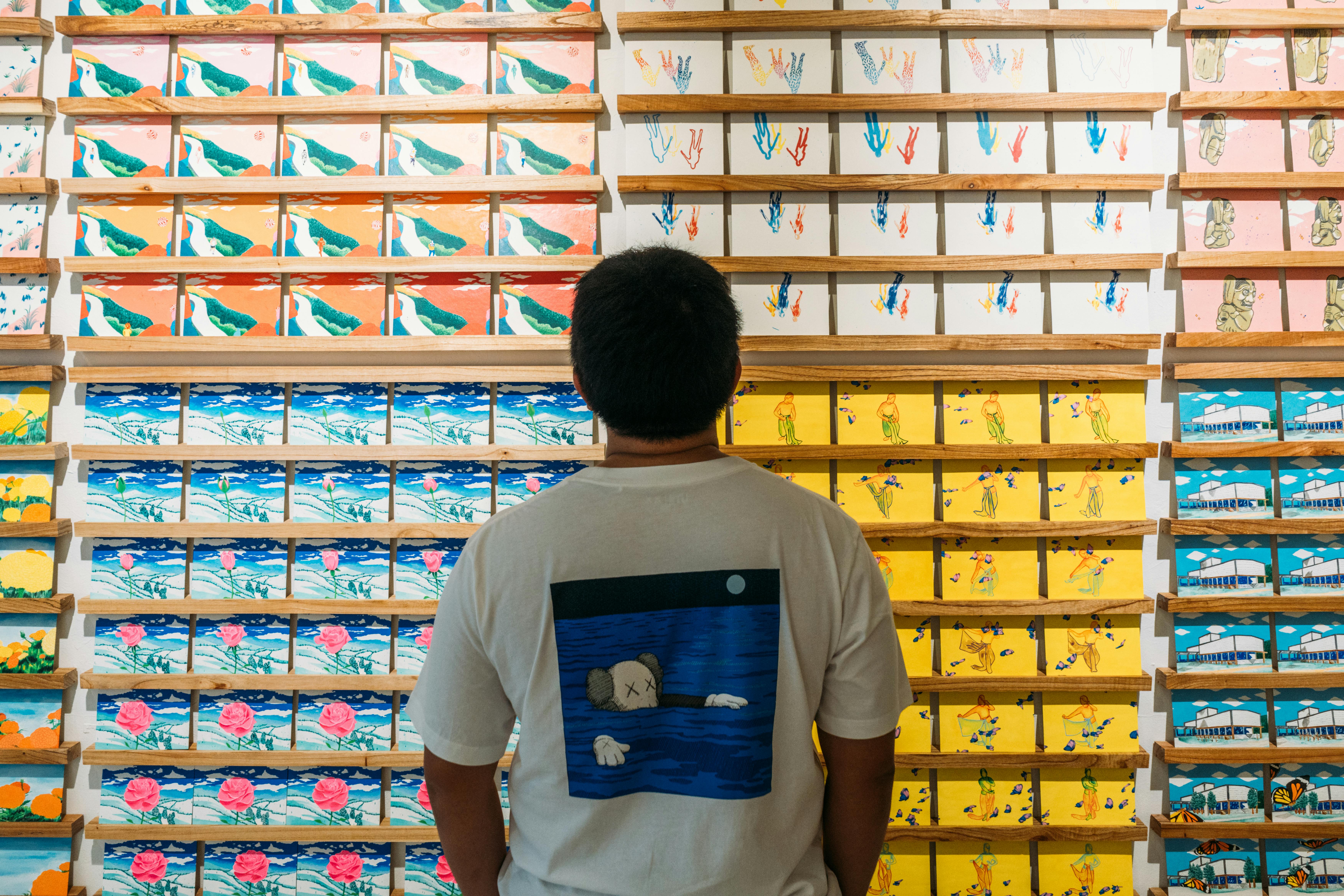 Man stands in front of vibrant wall art exhibit, appreciating the colorful patterns.