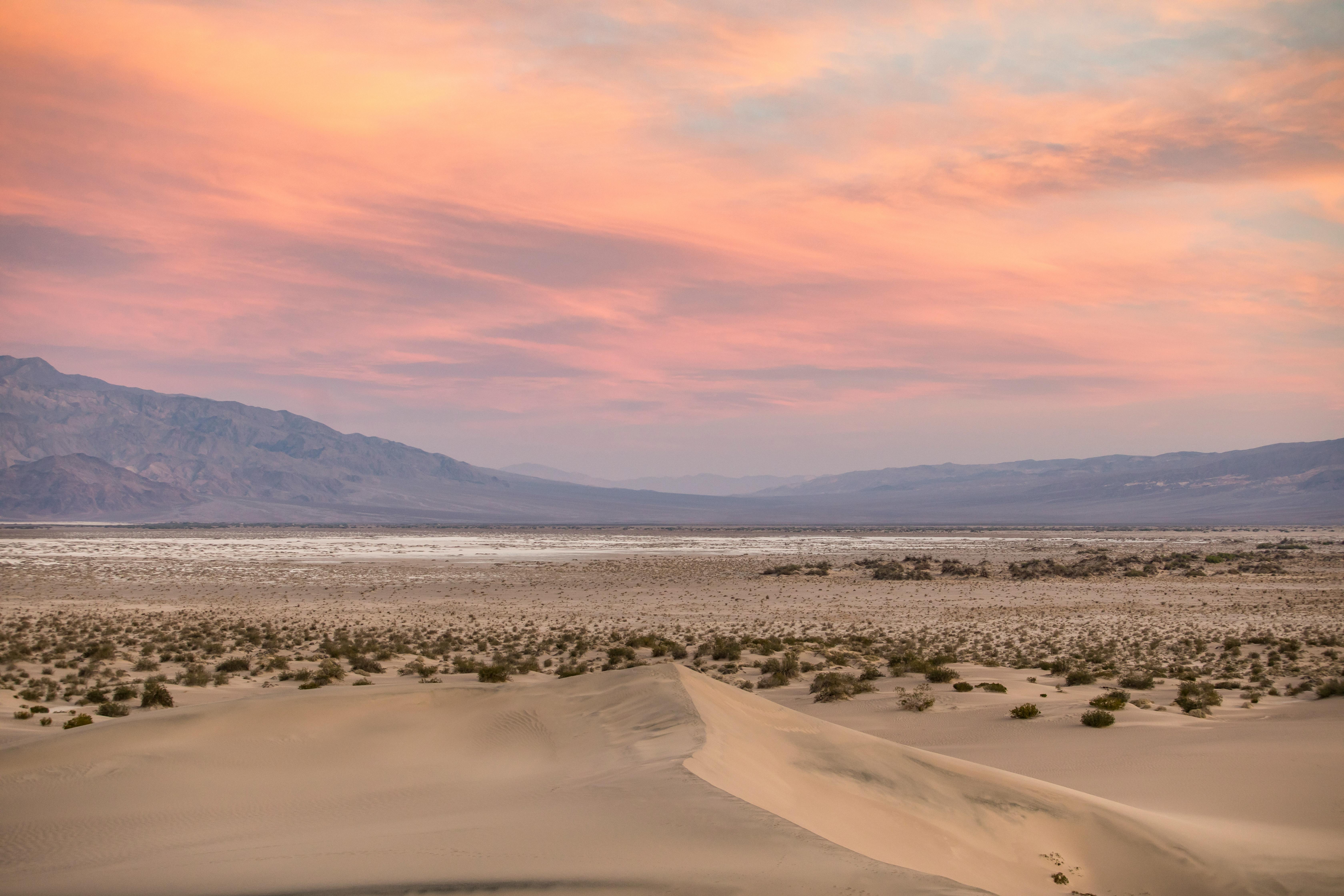 Vibrant sunset over desert landscape with sand dunes and mountains in the distance.
