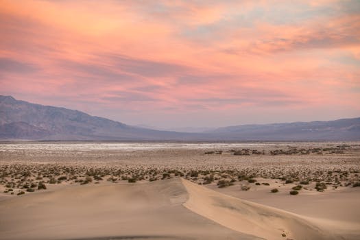 Vibrant sunset over desert landscape with sand dunes and mountains in the distance.