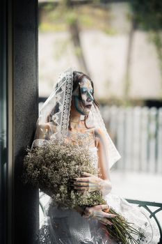 A woman in Dia de los Muertos makeup and attire stands gracefully holding flowers in Mexico City.