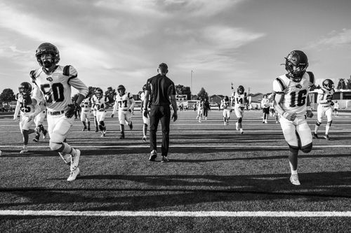 Free Black and white photo of a high school football team running on the field, showcasing teamwork and intensity. Stock Photo