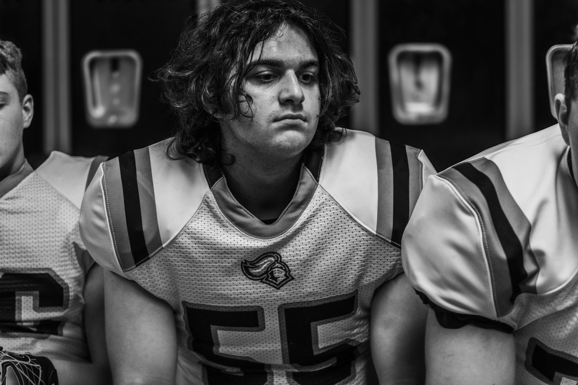 Focused portrait of a young football player in uniform inside a locker room.