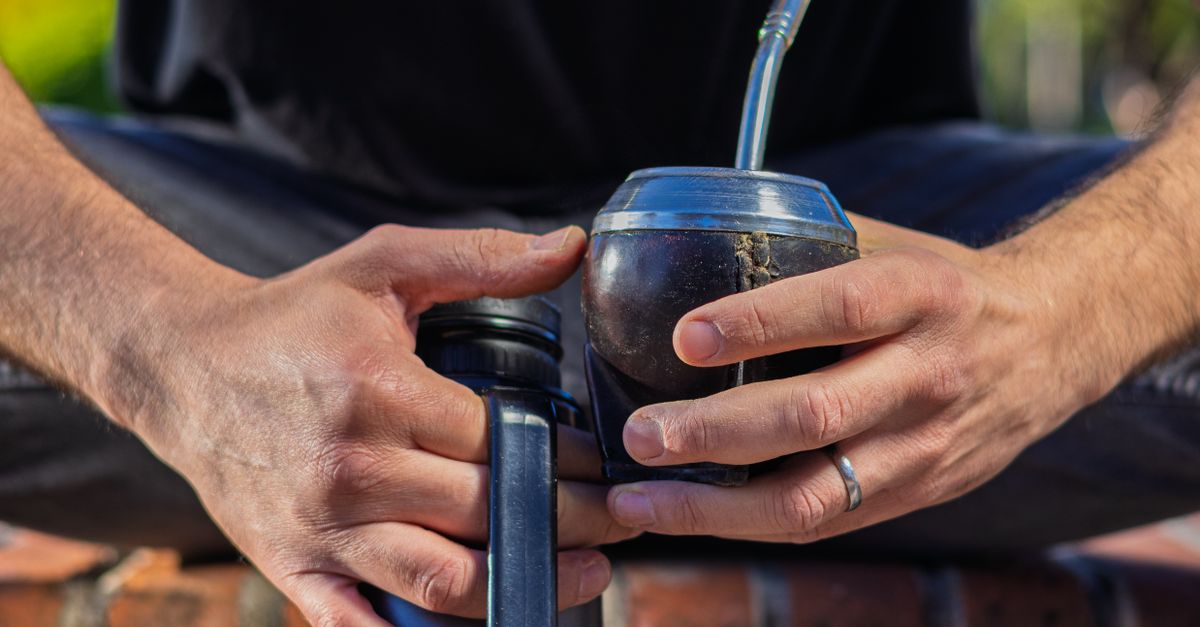 Close-up of man preparing yerba mate drink with thermos and cup in an outdoor setting.