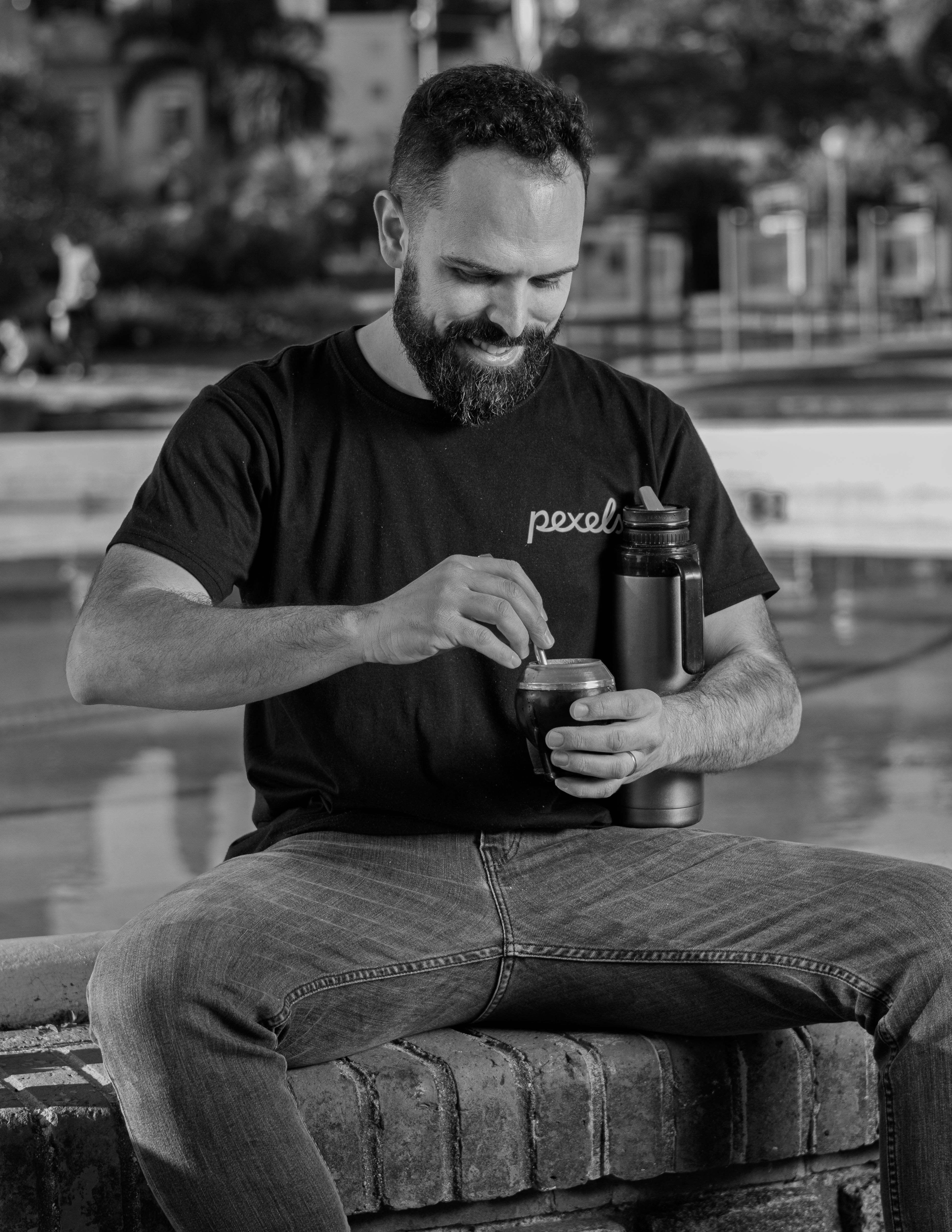 Black and white photo of a man preparing traditional mate drink outdoors.