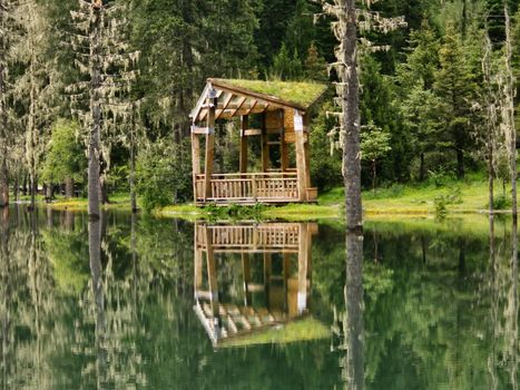 Peaceful lakeside pavilion surrounded by lush forest with a mirror reflection in the water.