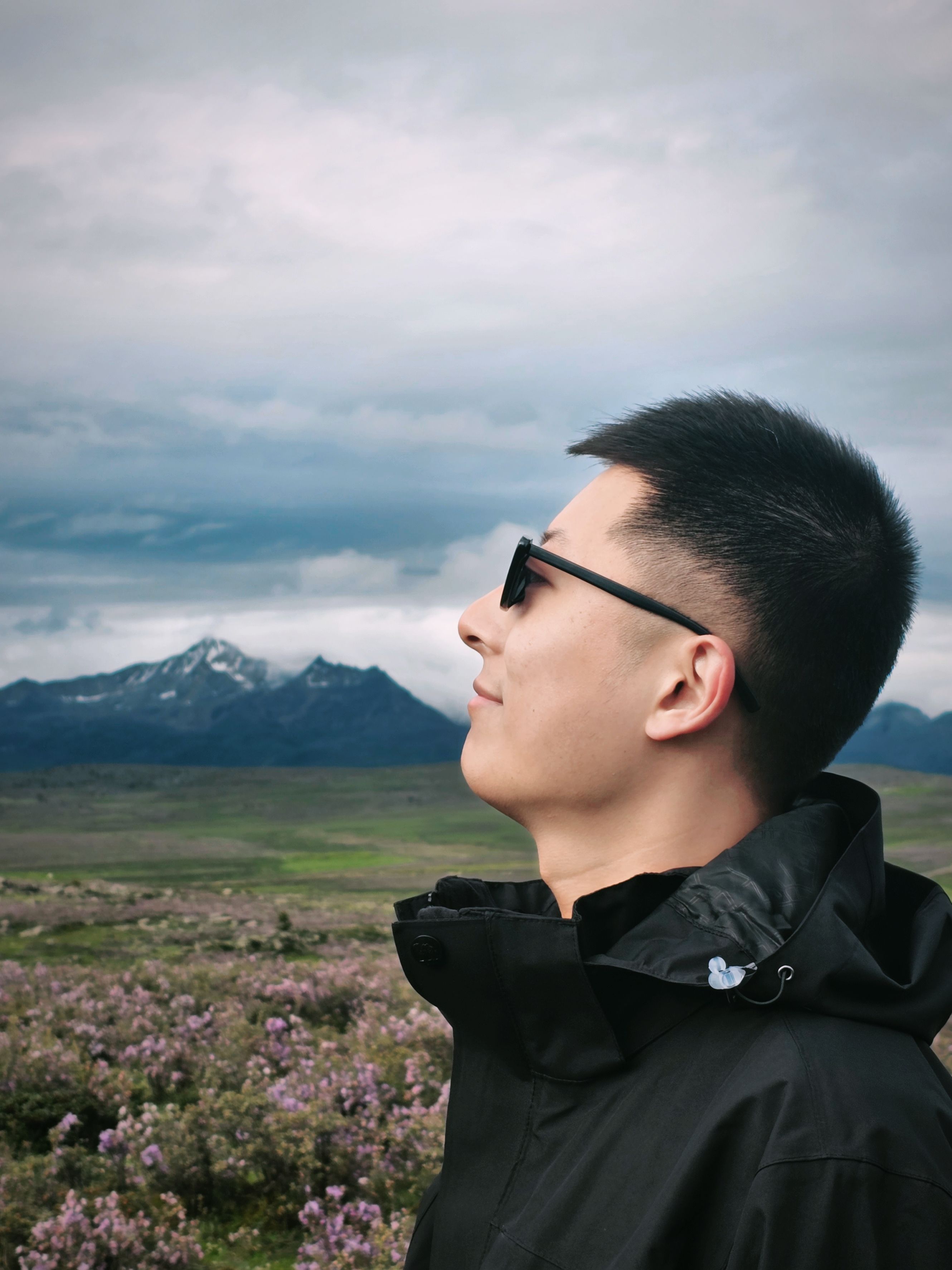 Man in sunglasses enjoying a mountain view in a field of wildflowers.