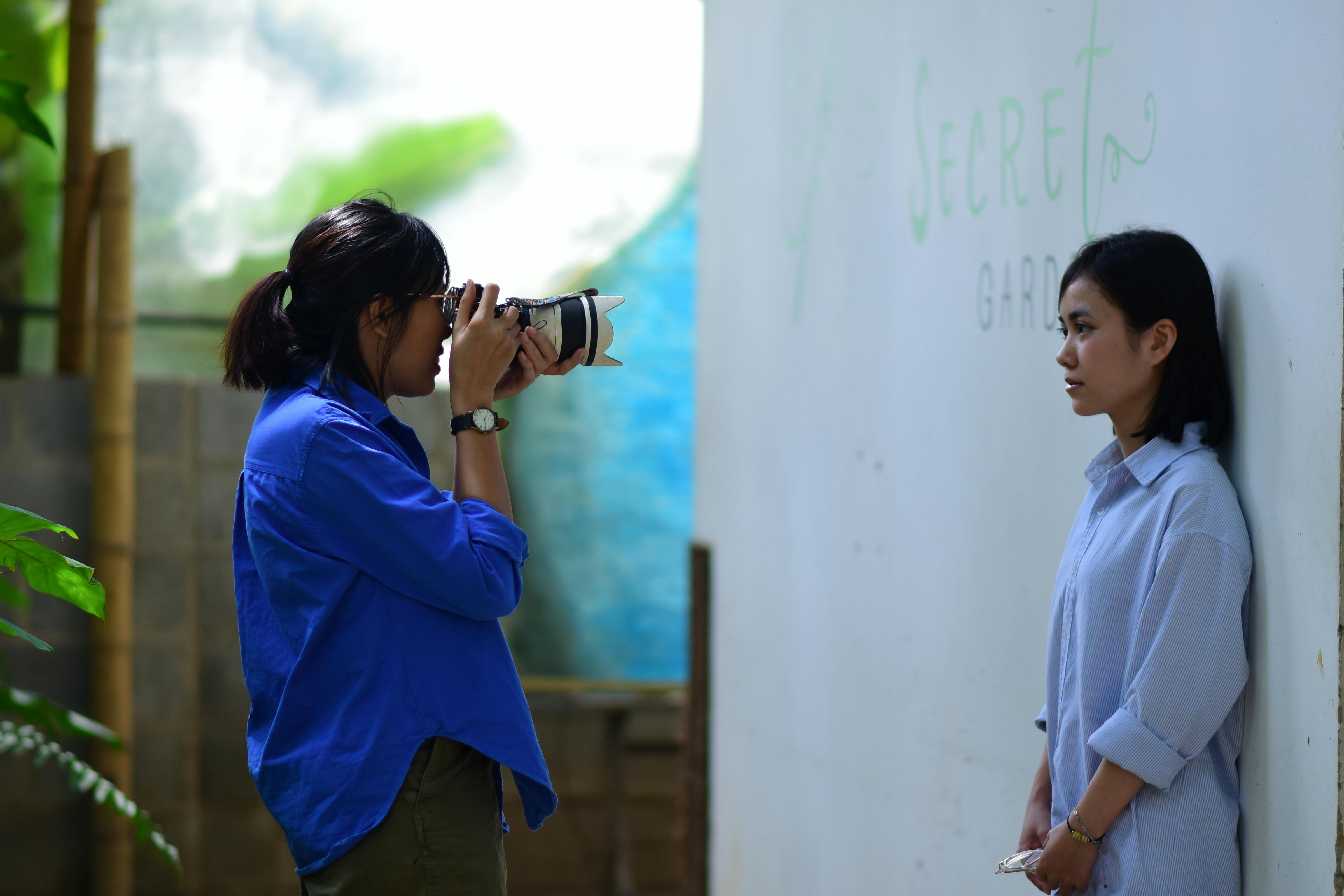 A photographer takes a portrait of a woman in an outdoor setting with a "Secret Garden" backdrop.
