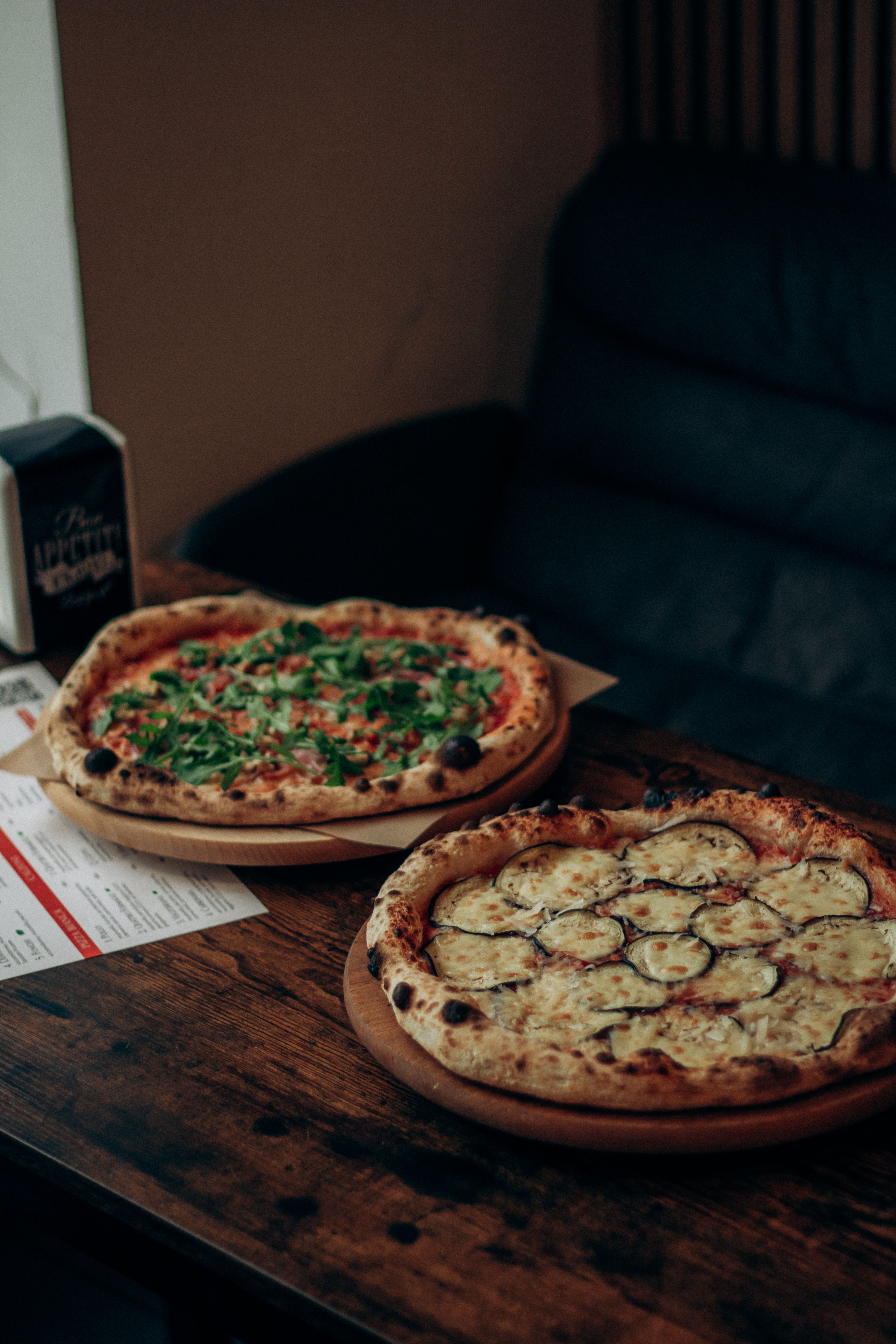 Two freshly baked pizzas with toppings on a wooden table in a cozy setting.