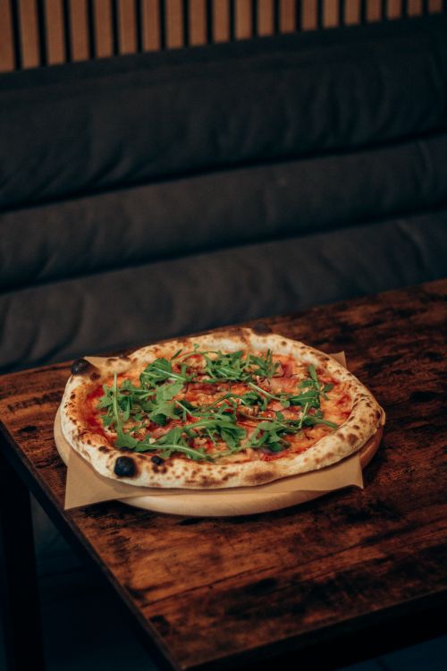 Free A freshly baked wood-fired pizza topped with arugula served on a rustic wooden table. Stock Photo