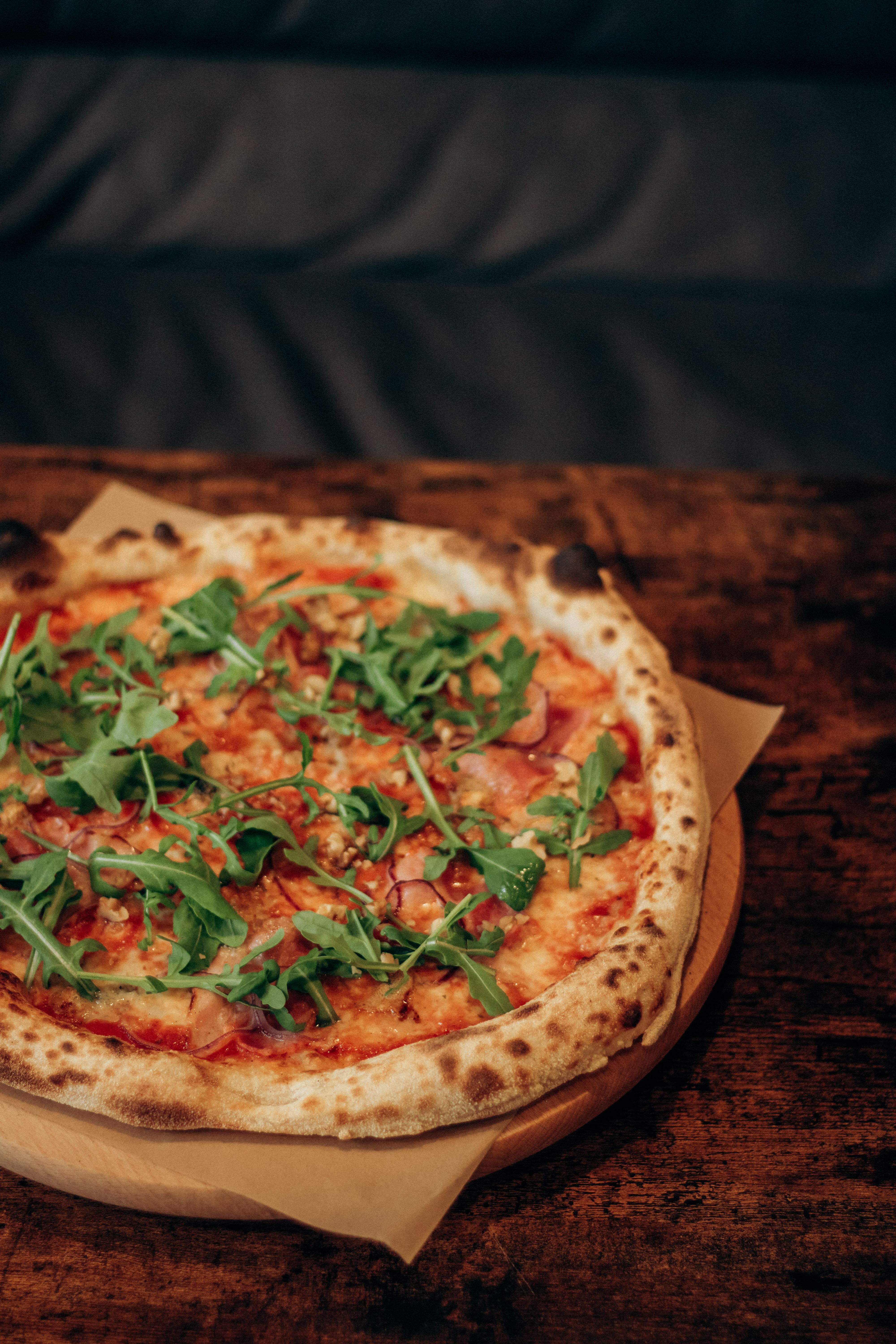 Ilmainen Herkullinen puu-uunissa paistettu pizza, jonka päällä on tuoretta rucolaa, maalaismaisella pöydällä. Kuvapankkikuva