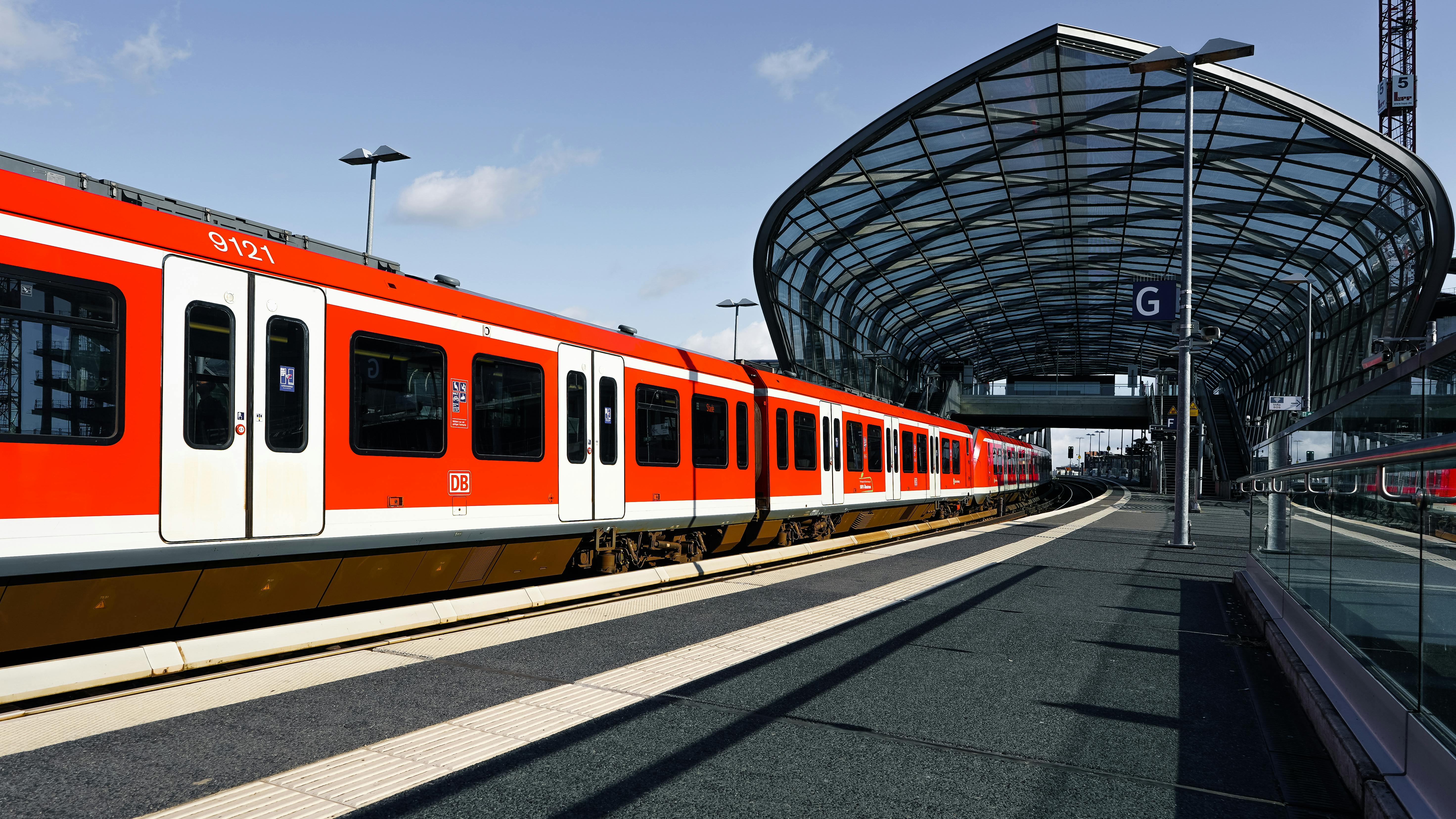 Explore the modern and futuristic architecture of Hamburg's iconic train station with a vibrant red commuter train.