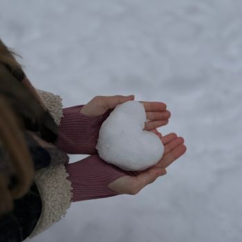 Hands holding a heart-shaped snowball on a winter day, symbolizing love.