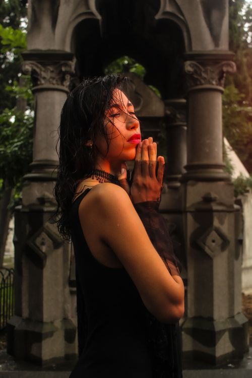 Free A woman in deep thought stands by ornate gothic architecture in a cemetery. Stock Photo