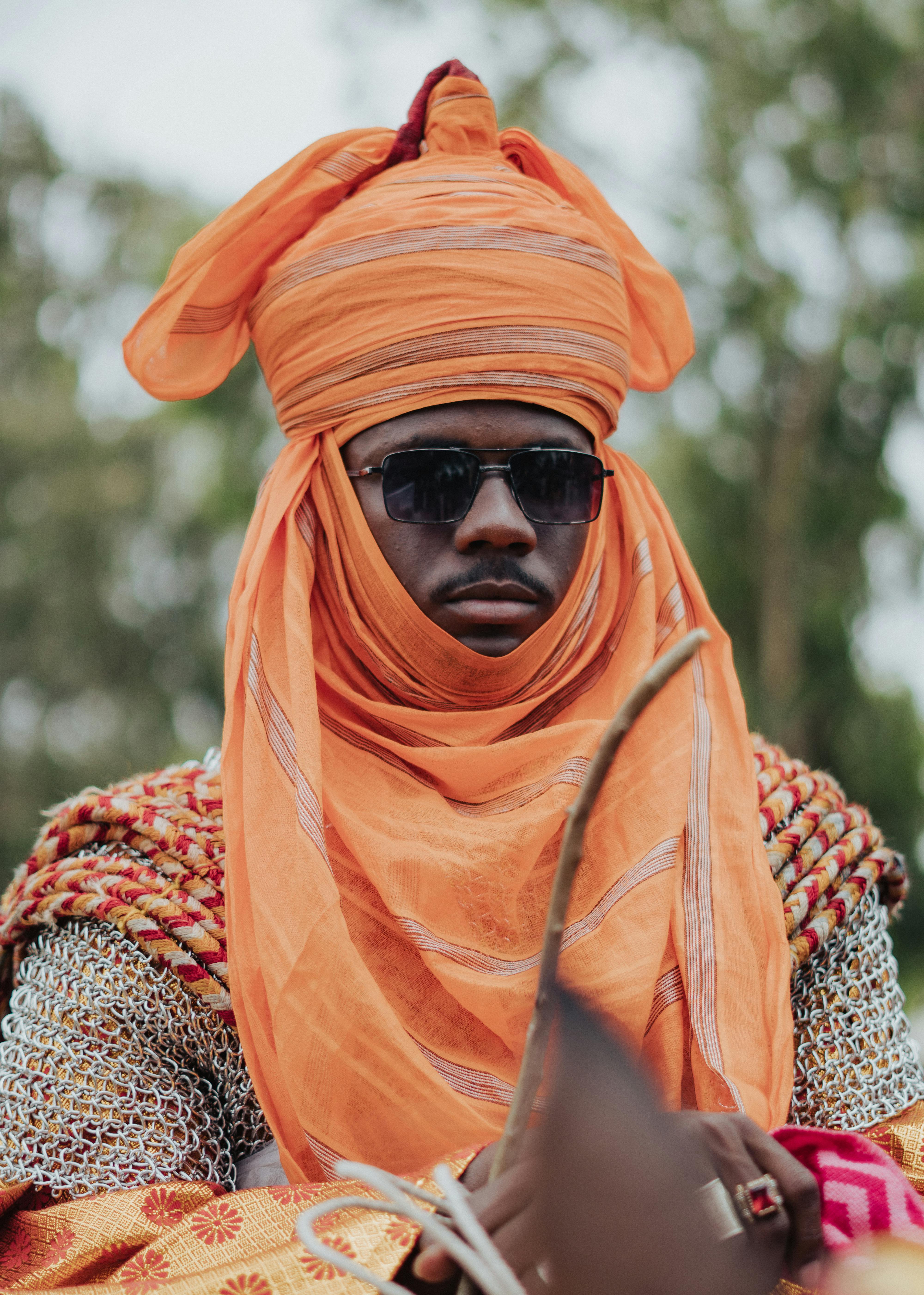 A man wearing traditional orange attire and sunglasses, showcasing cultural heritage.