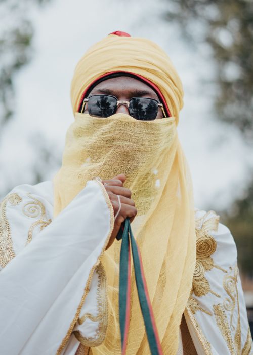 Free Man in ornate traditional attire with a yellow veil and sunglasses, outdoors. Stock Photo