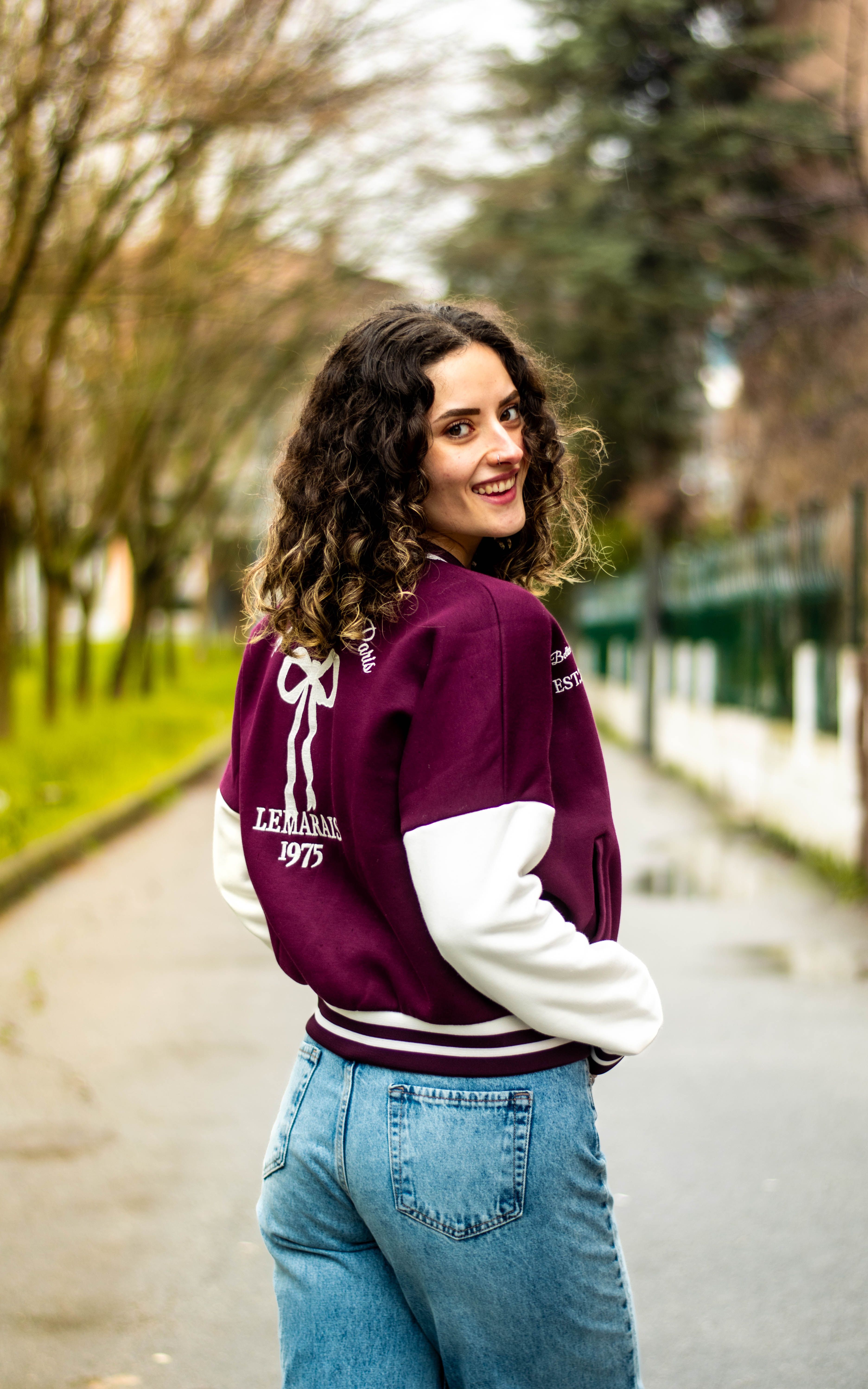 Smiling Woman in Varsity Jacket Outdoors · Free Stock Photo