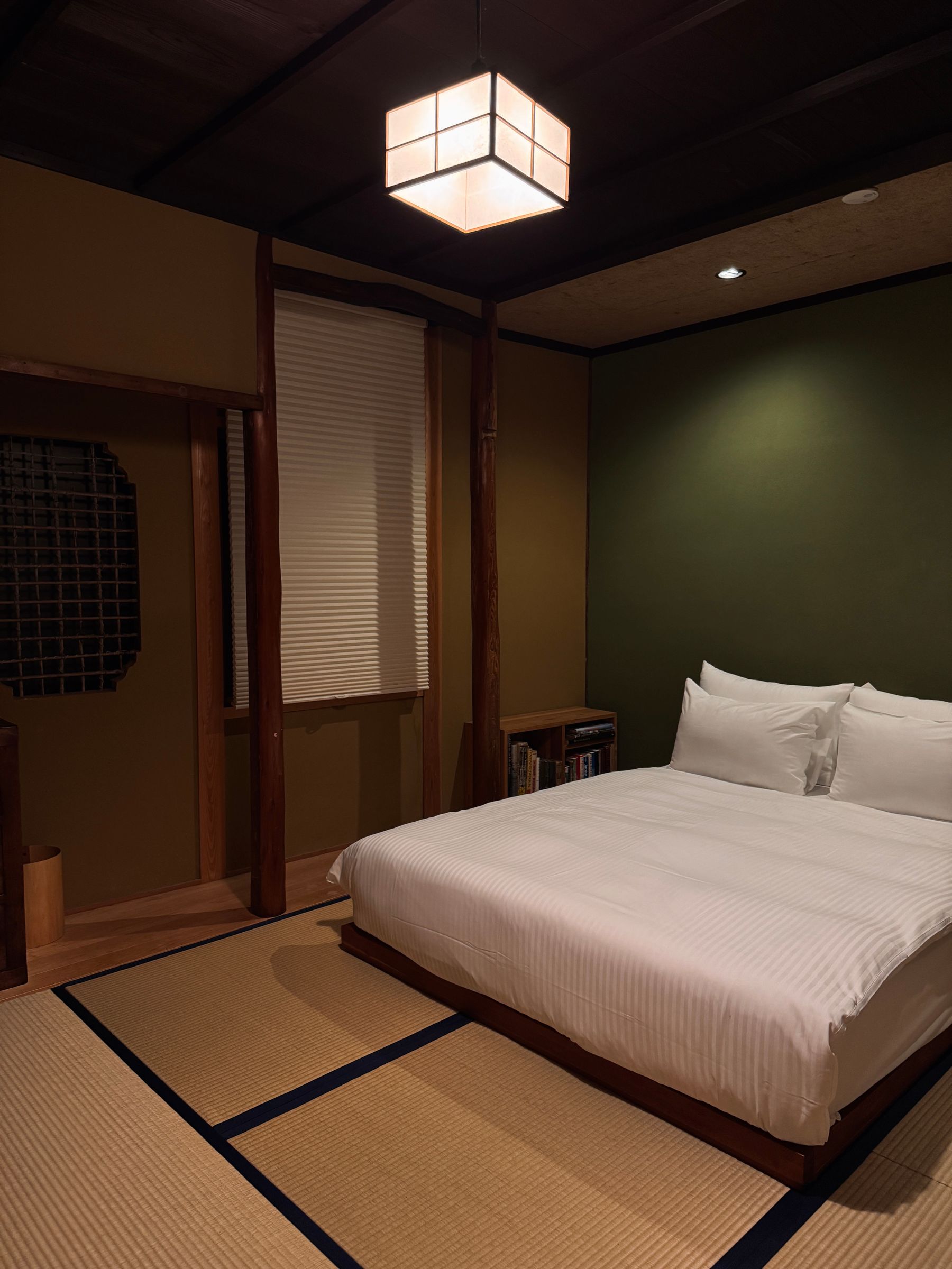 Japanese-style bedroom with a white bed, tatami-grid floor, broad shoji panels, dark timber and warm reading lights
