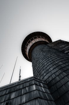 A low angle view of a tower with shingled exterior and antennas against a moody sky.