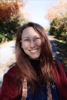 A cheerful young woman in glasses enjoys a sunny fall day outdoors.