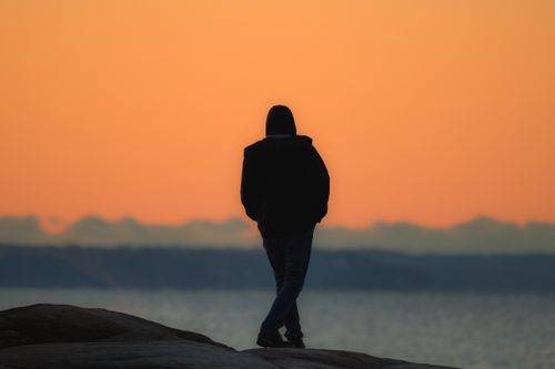 Free Silhouette of a person watching a sunrise over Long Island Sound from a rocky shoreline. Stock Photo