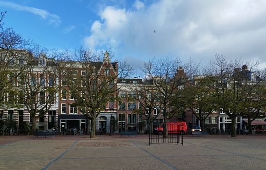 Amsterdam canal houses under a bright blue sky with bare winter trees lining the street.