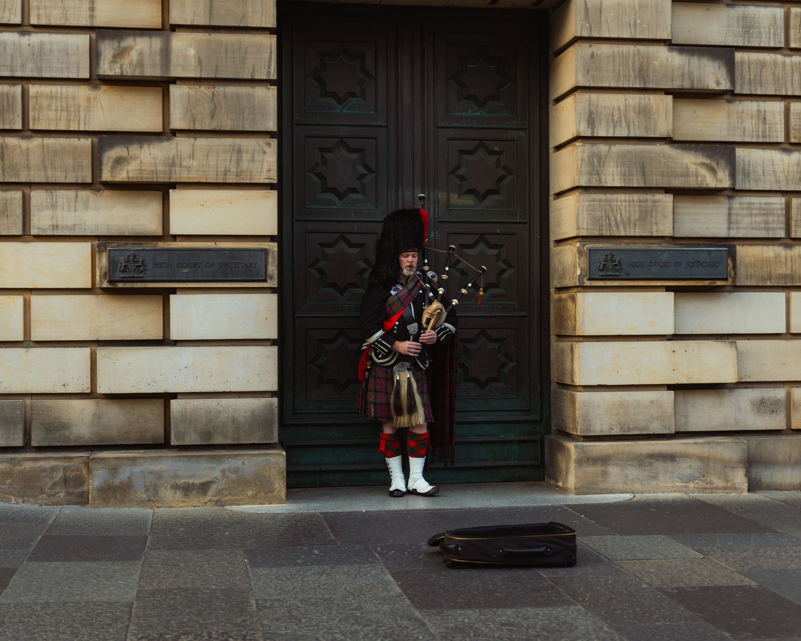 A bagpiper in traditional attire plays outside a historic building in Edinburgh, Scotland.