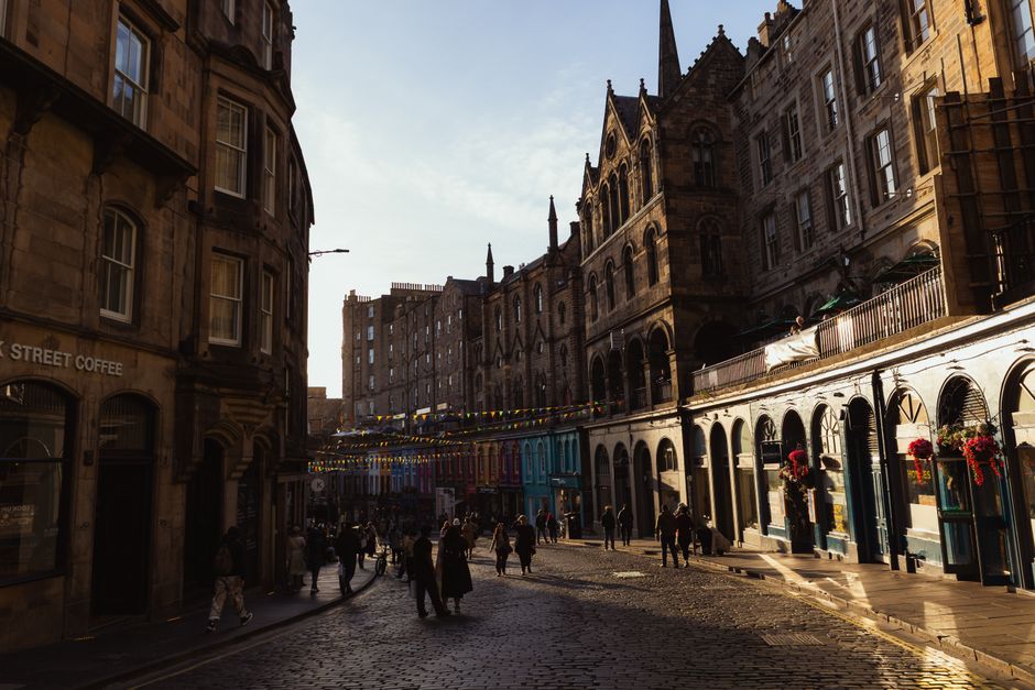 Victorian buildings and a bustling street scene captured in Edinburgh, Scotland, illuminated by golden sunlight.
