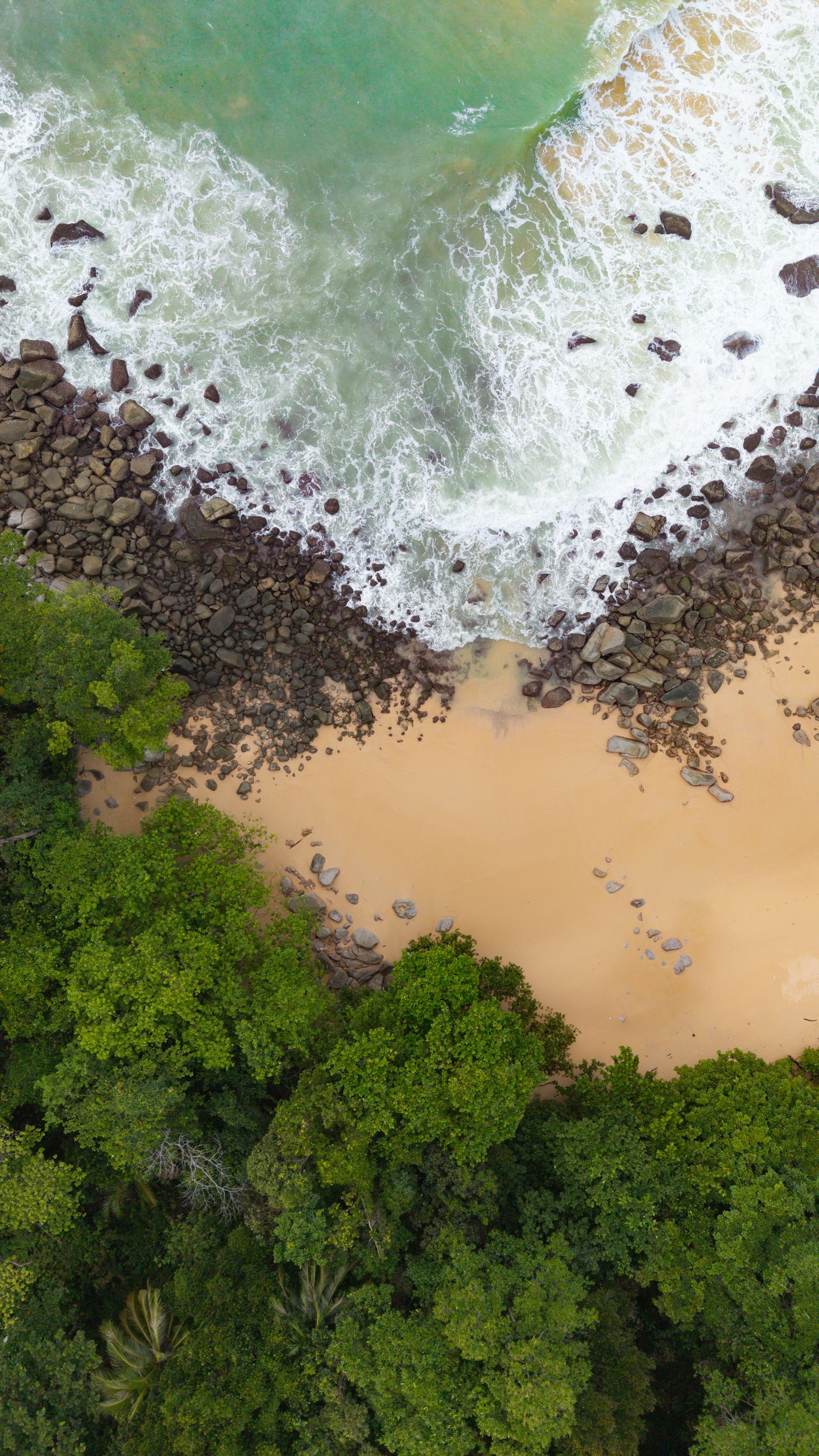 Aerial view of tropical shoreline near Cape Panwa, Phuket, Thailand, with green forest meeting the sea.
