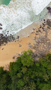 Stunning aerial view of a sandy beach, rocks, and lush forest in Phuket, Thailand.