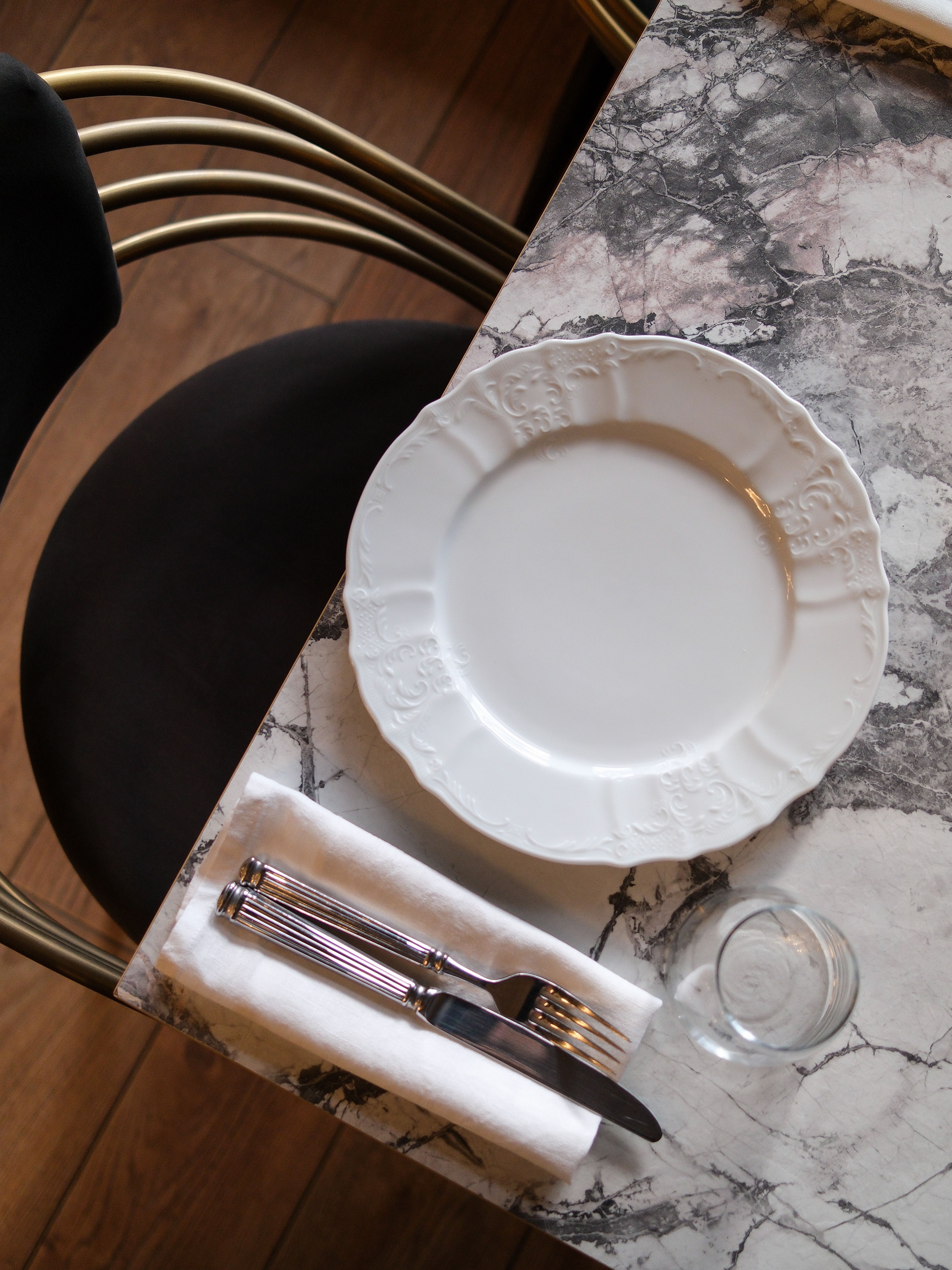 Top view of a stylish marble table setting with plate, cutlery, and a glass.