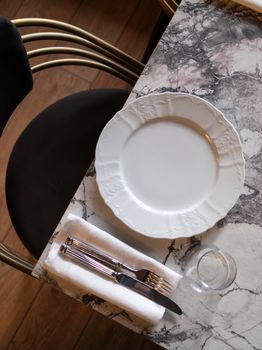 Top view of a stylish marble table setting with plate, cutlery, and a glass.