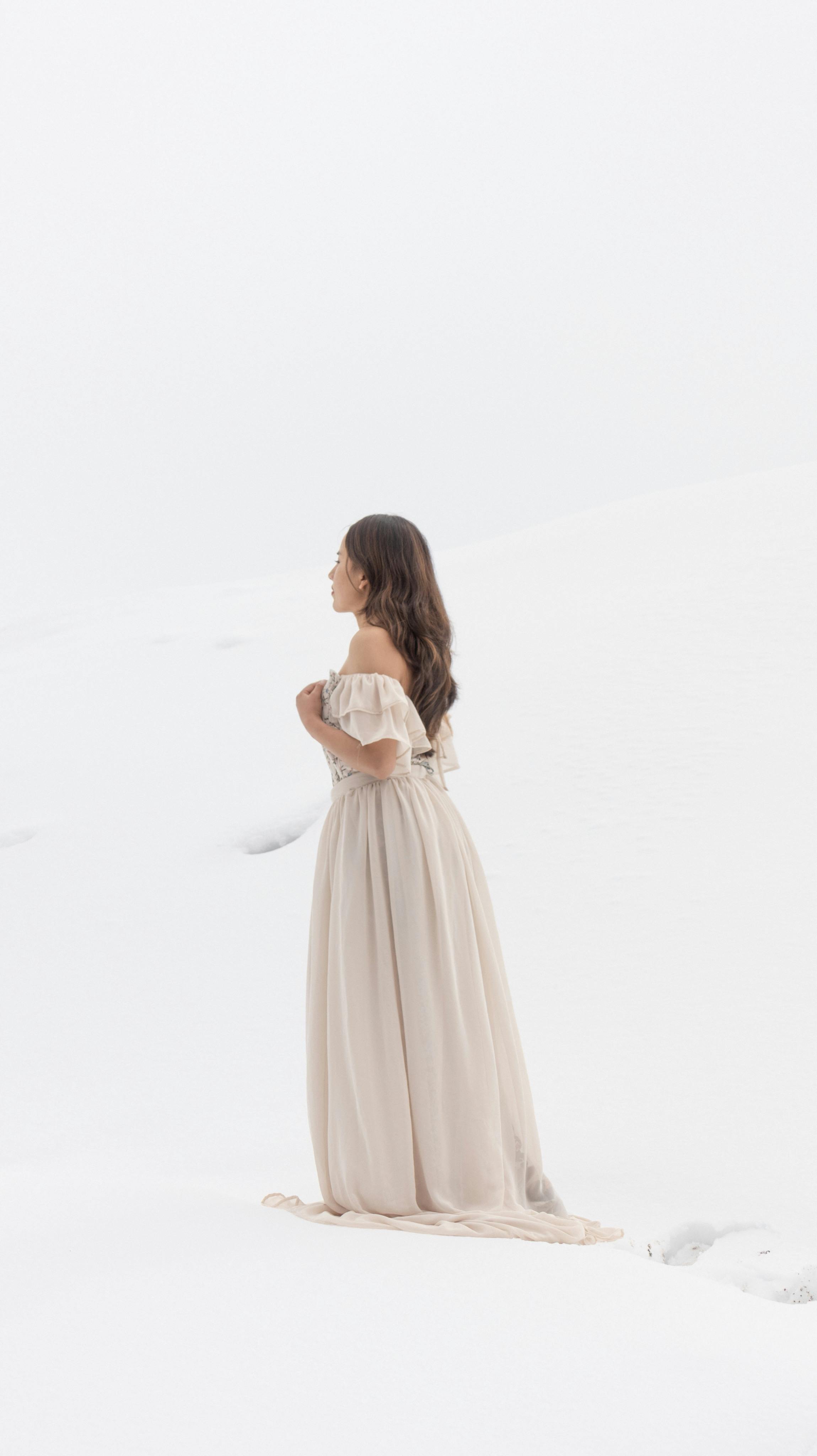A woman in a flowing gown stands gracefully in a serene snowy landscape.
