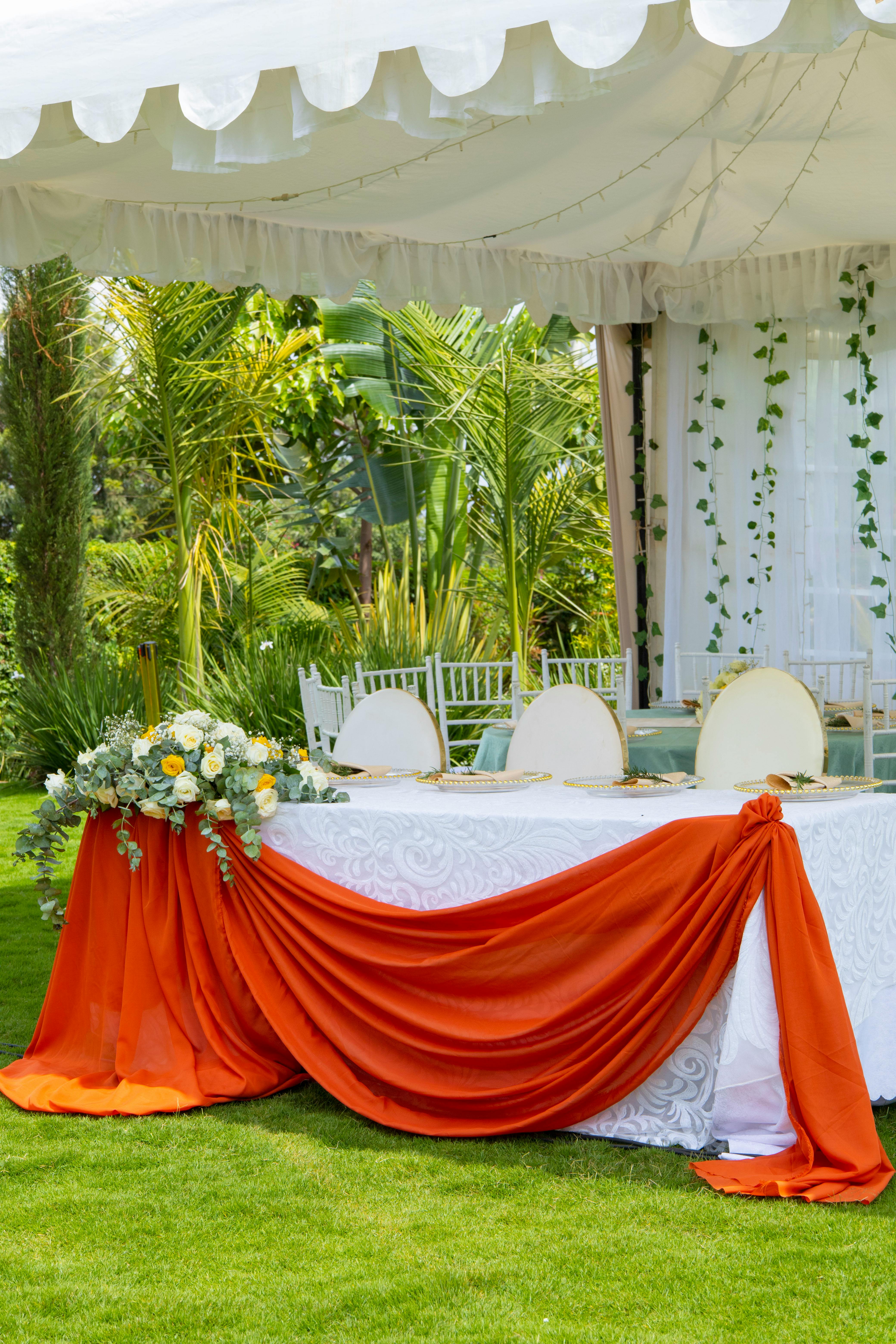 Beautifully decorated outdoor wedding table with orange drapery and green surroundings.