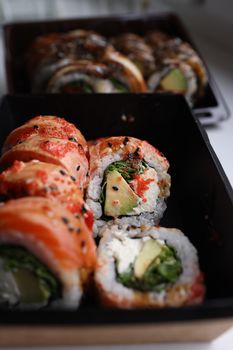 Close-up of gourmet sushi rolls with fresh avocado, salmon, and sesame seeds, presented in a black tray.
