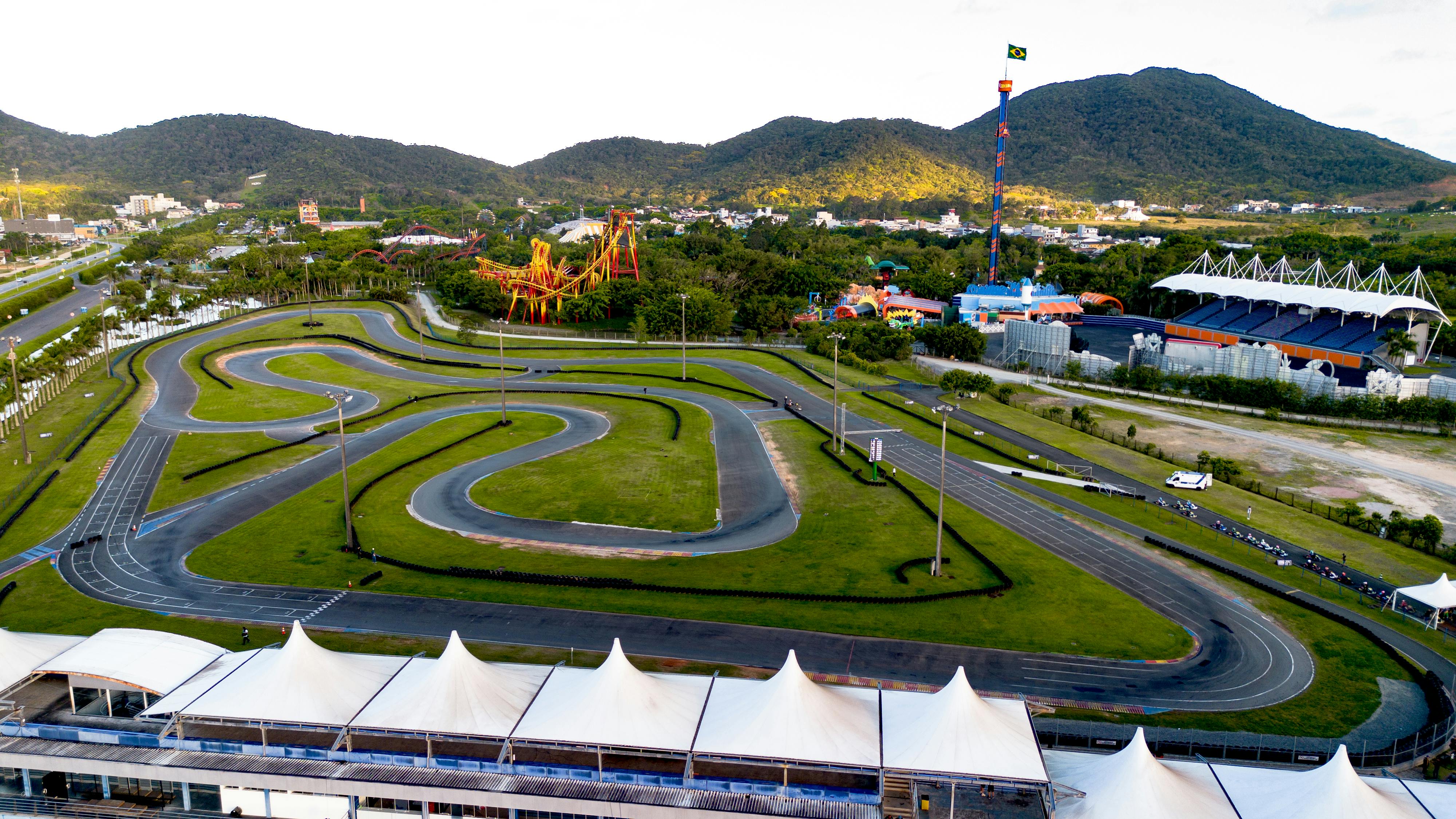 Aerial view of a kart racing track near an amusement park with scenic greenery and blue skies.