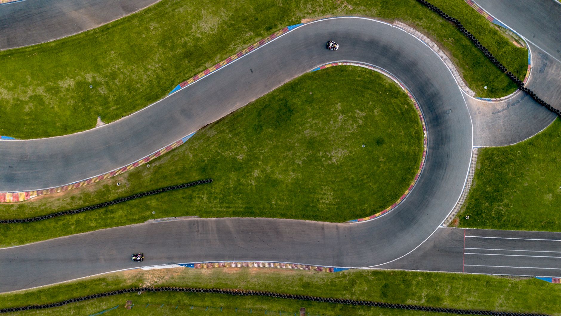 Drone captures an aerial view of a kart racing track with vibrant green surroundings and active go-karts.
