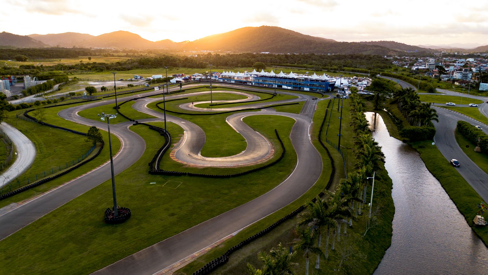 An aerial view captures a winding go-kart track and lush green landscape at sunset.
