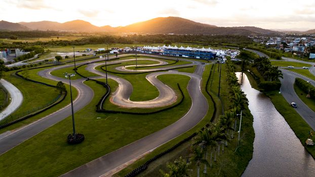 An aerial view captures a winding go-kart track and lush green landscape at sunset.