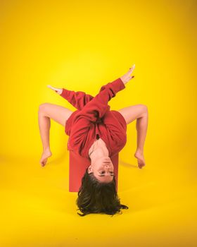 Upside-down woman in red sweater against a vivid yellow background, showcasing flexibility and creativity.