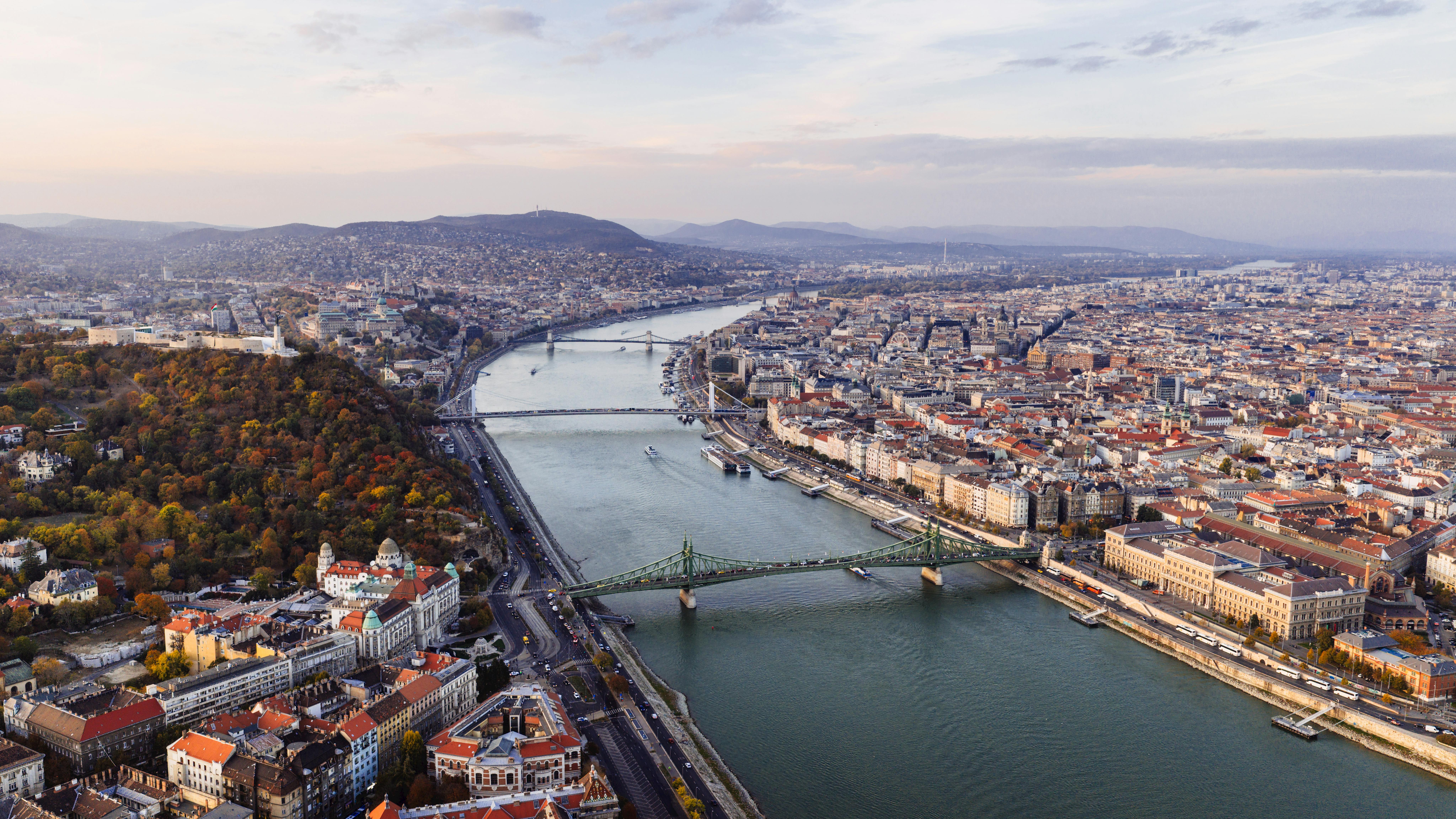grátis Bela vista aérea de Budapeste com o Rio Danúbio e pontes icônicas ao pôr do sol. Foto profissional