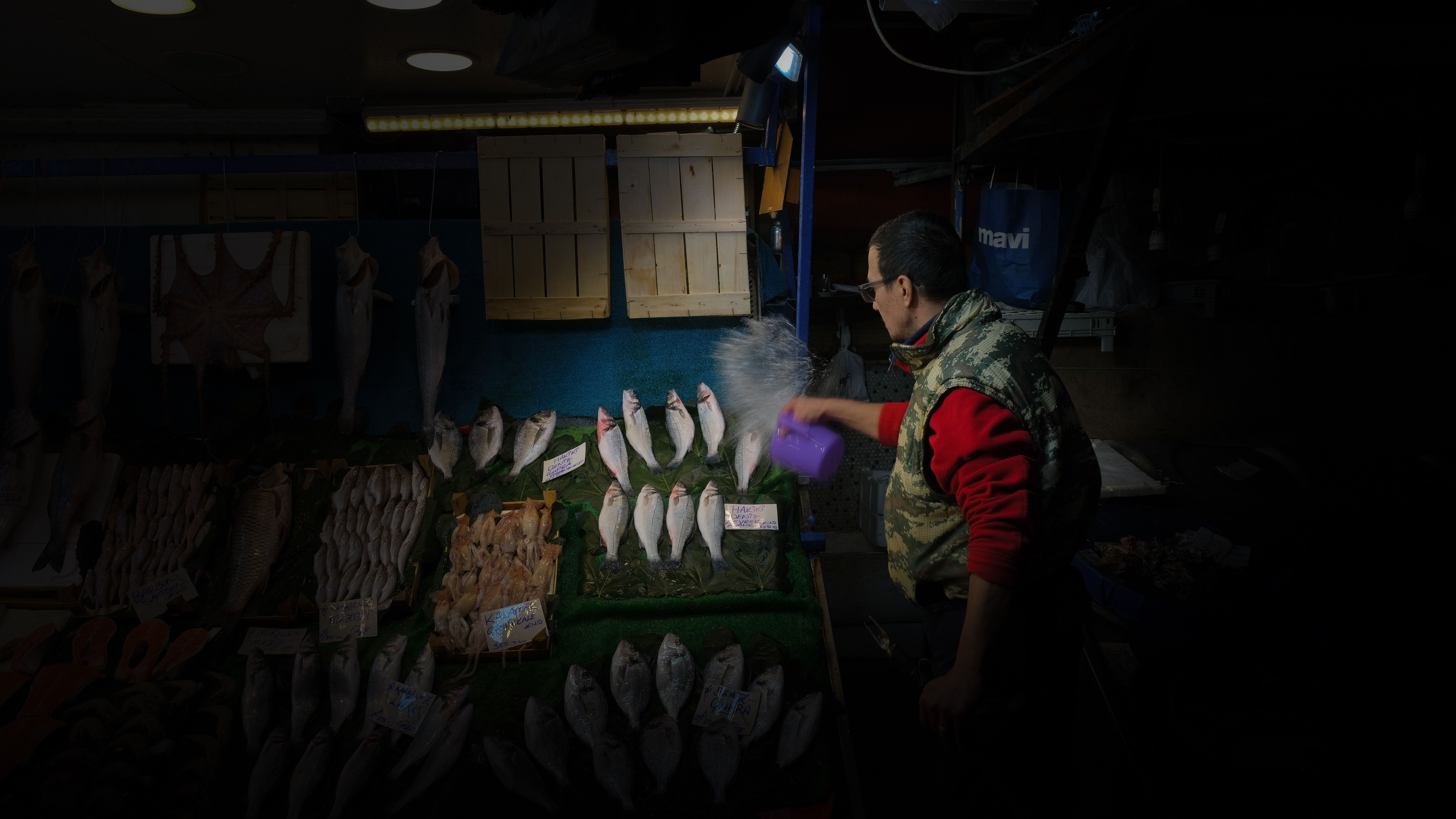A vendor at an Istanbul fish market arranging fresh fish on display, using a spray bottle.