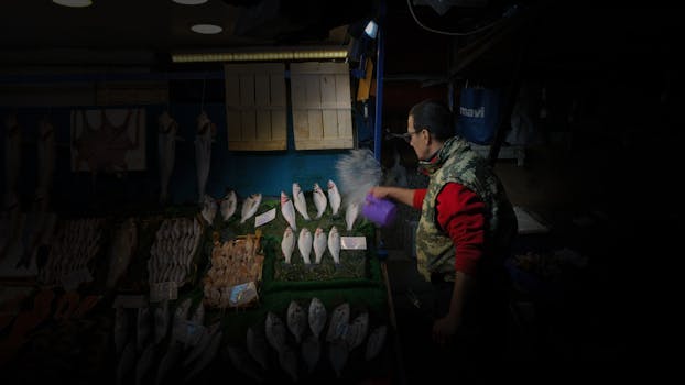 A vendor at an Istanbul fish market arranging fresh fish on display, using a spray bottle.